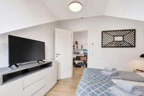 Ein modernes Schlafzimmer mit einem Flachbildfernseher auf einem Standfuß, einem Bett mit gemusterten Bettbezügen und einem dekorativen Wandbild.