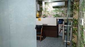Un área de recepción con un mostrador, una silla, una pequeña estatua de Buda y una pared con diseño de ladrillo y plantas.