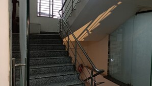 Una escalera con barandales metálicos, un extintor y una puerta de cristal con marco de metal.