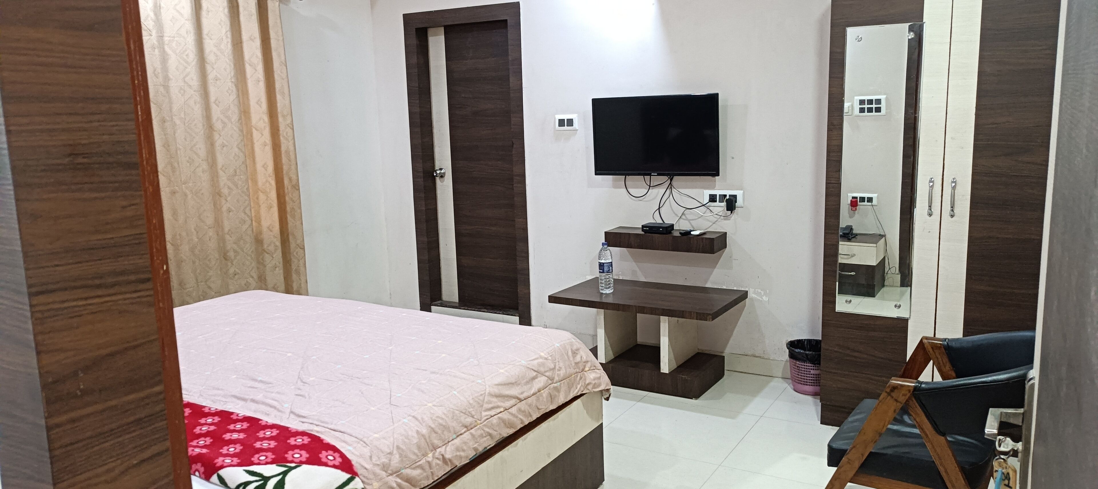 A bedroom with a bed, a desk, a TV, a mirror, and a wardrobe.