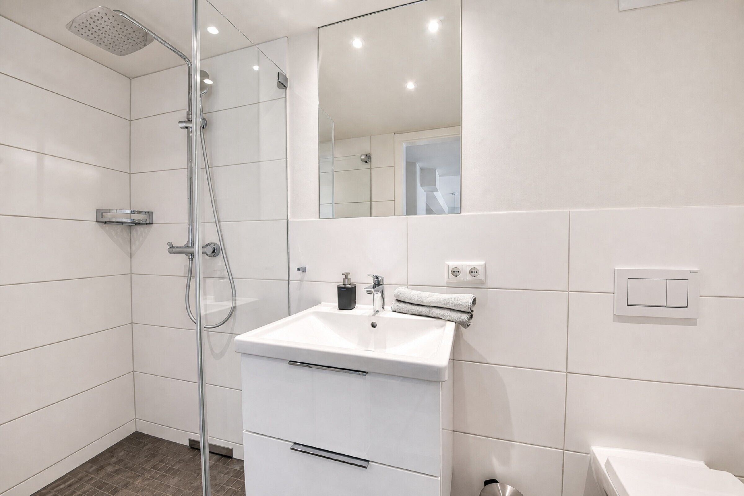 Une salle de bain moderne avec une douche à parois de verre, un lavabo blanc avec une serviette et un miroir qui reflète la pièce.