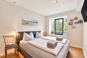 Ein modernes Schlafzimmer mit zwei Betten, einem Fenster mit Blick auf Bäume und einem wandmontierten Flachbildfernseher.