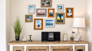 A room with a wooden cabinet, a plant, a lamp, and a wall decorated with various framed pictures.