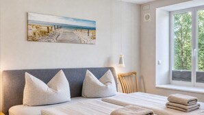 A bedroom with a bed, pillows, a headboard, a window with a view, and a painting on the wall.