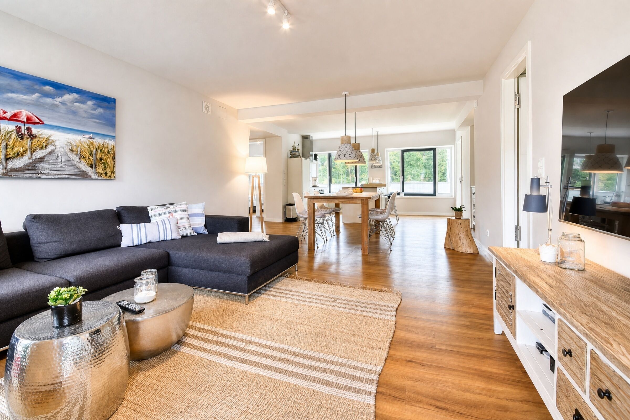 Un salon moderne avec un canapé d’angle, un coin repas et une cuisine visible au fond.