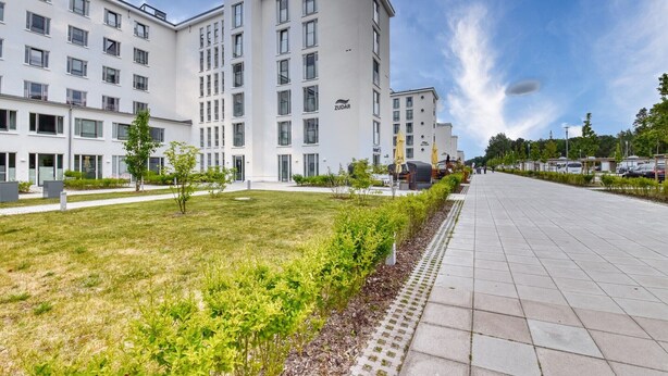 A modern hotel with multiple floors, a well-maintained lawn, and a paved walkway.
