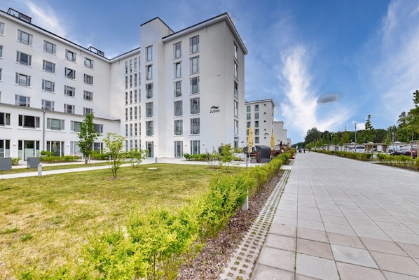 Ein modernes Hotel mit mehreren Etagen, einem gepflegten Rasen und einem gepflasterten Weg.