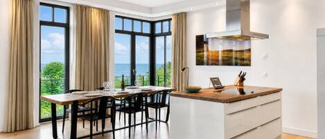 A modern kitchen with a central island, large windows, and a view of the sea.