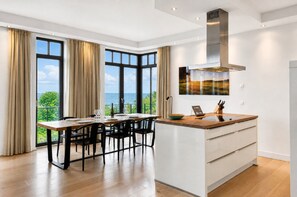 A modern kitchen with a central island, large windows, and a view of the sea.