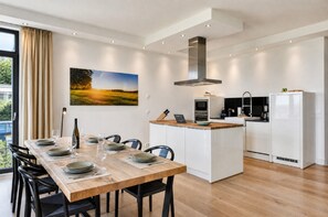 A modern kitchen with white cabinetry, a central island, and a dining area with a wooden table and chairs.