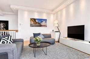 A modern living room with a grey sofa, a coffee table with a vase of flowers, a flat-screen TV, and a painting of a beach scene.