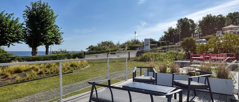 An outdoor seating area with tables and chairs, a wooden deck, and a view of the sea.