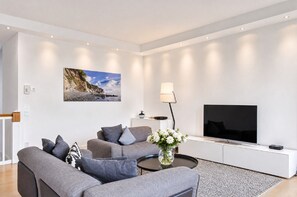 Una sala de estar moderna con un sofá gris, un televisor de pantalla plana y un cuadro de un paisaje costero.
