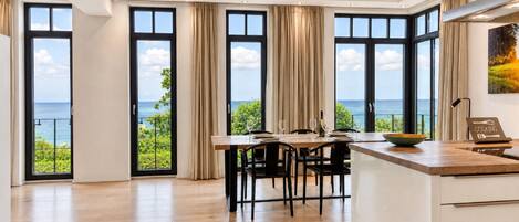 A modern kitchen with large windows, a dining area, and a view of the sea.