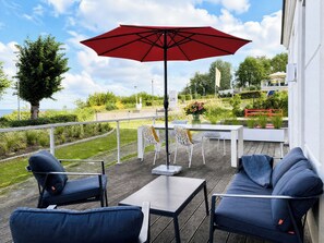 An outdoor patio with a table and chairs, a red umbrella, and a view of the sea.