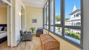 Una habitación con ventanas amplias, un banco de mimbre, un sofá y una silla.
