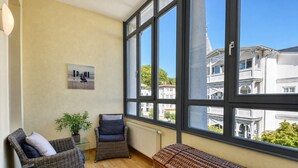 Una habitación con amplios ventanales, muebles de mimbre, una planta en maceta y vistas a la ciudad.
