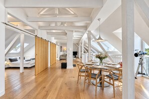 A spacious loft with high ceilings, wooden flooring, a dining area with a table set for four, and a telescope on the right. - Welcome to our vacation apartment in the heart of Putbus at the Circus! (Putbus)
