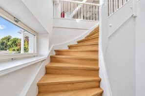 Una escalera de madera con barandillas blancas que conduce a un rellano con un ventanal que da a la vegetación.