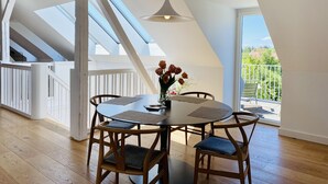 Ein Essbereich mit rundem Tisch, vier Holzstühlen, einer Blumenvase und einer Pendelleuchte.