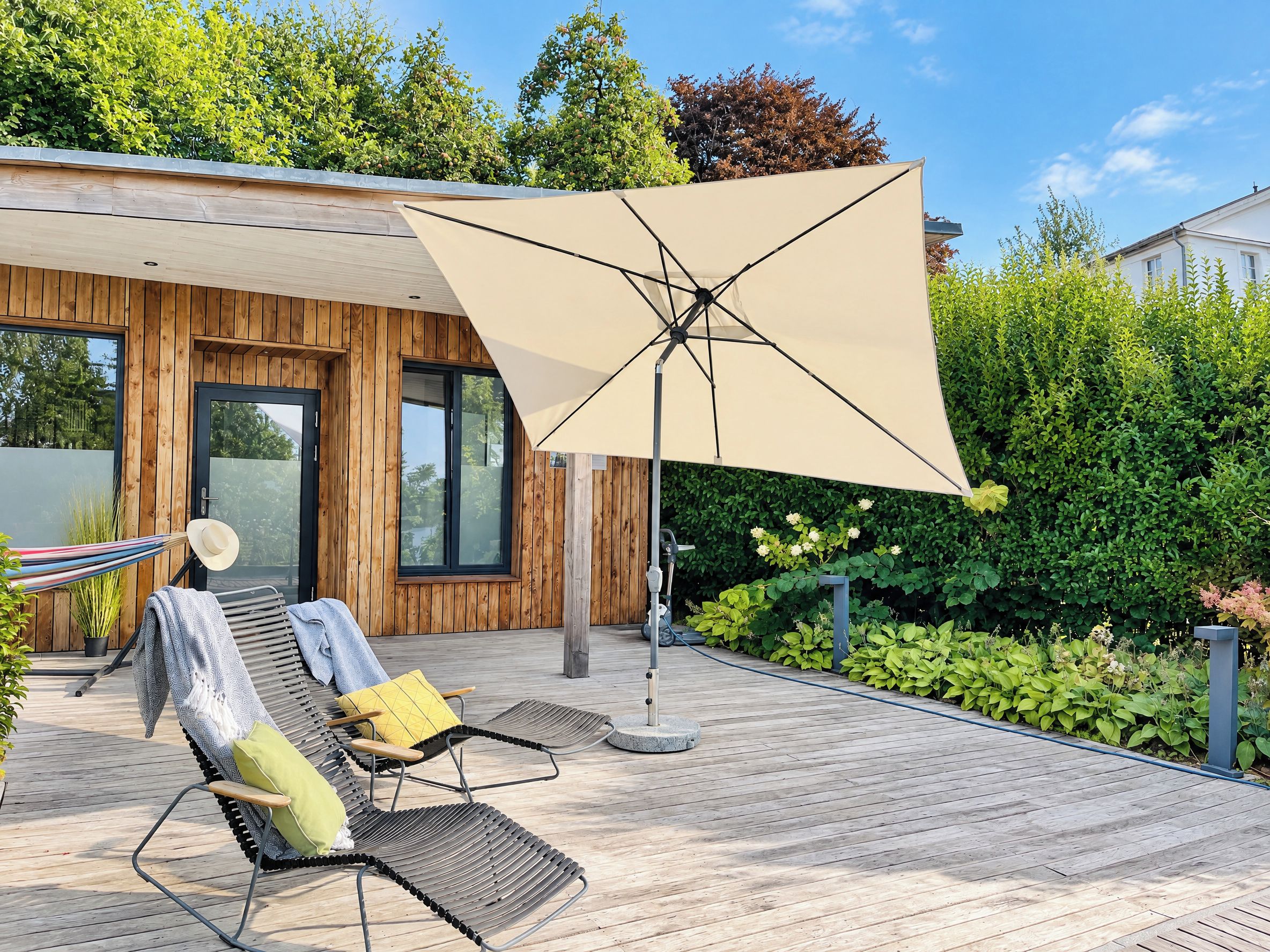 Een houten terras met buitenmeubilair, een grote parasol en uitzicht op een modern gebouw.
