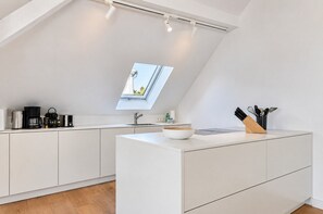 Una cocina moderna con tragaluz, muebles blancos y una isla central con un bol y utensilios.