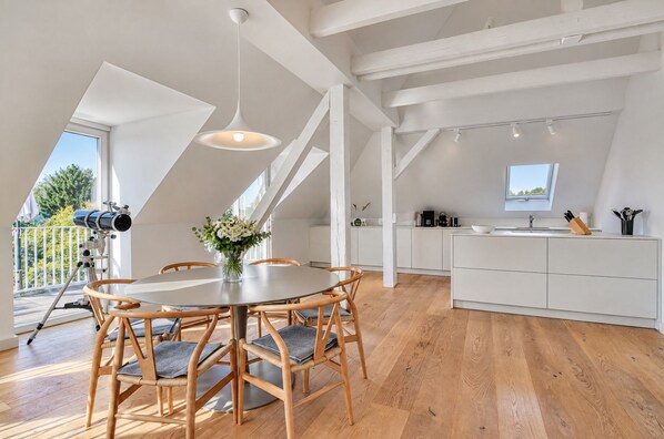 Una cocina moderna con muebles blancos, un comedor con sillas de madera y un tragaluz grande.