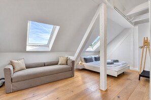 Un dormitorio estilo loft moderno con techo inclinado, sofá, cama y tragaluz.