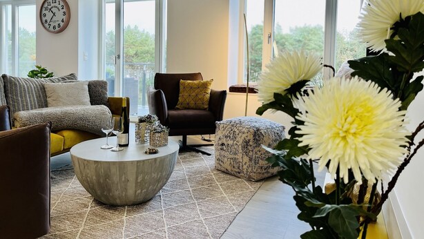Ein modernes Wohnzimmer mit einer Couch, einem Sessel, einem Couchtisch und großen Fenstern.