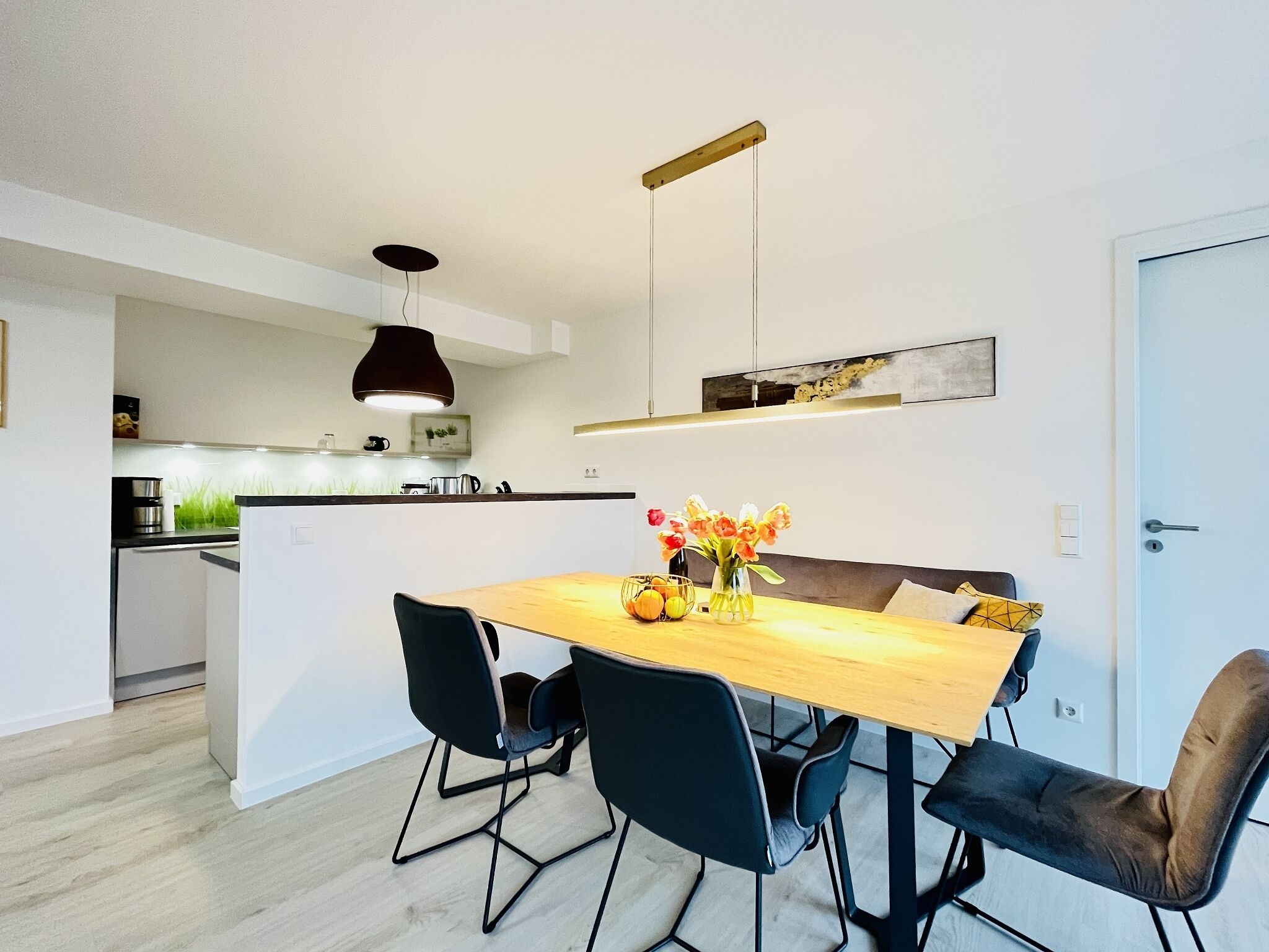 Una cocina moderna con una isla central, sillas negras y una mesa de comedor de madera con un florero.