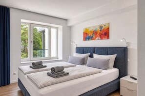 A modern bedroom with a large bed, a window with curtains, a painting on the wall, and a bedside table with a remote control. - "Haven of peace" in Prora: modern comfort, maritime flair right on the Baltic Sea beach (Prora)
