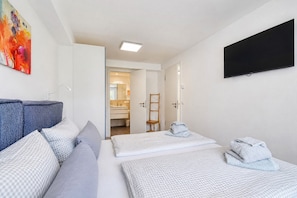 Habitación de hotel con cama, sofá, televisión y baño visible a través de una puerta abierta.
