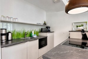 A modern kitchen with a built-in dishwasher, a coffee machine, and a hanging pot rack. - "Haven of peace" in Prora: modern comfort, maritime flair right on the Baltic Sea beach (Prora)