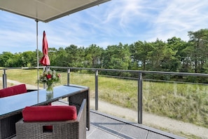 Un patio al aire libre con una mesa de vidrio, sillas de mimbre y un paraguas rojo.