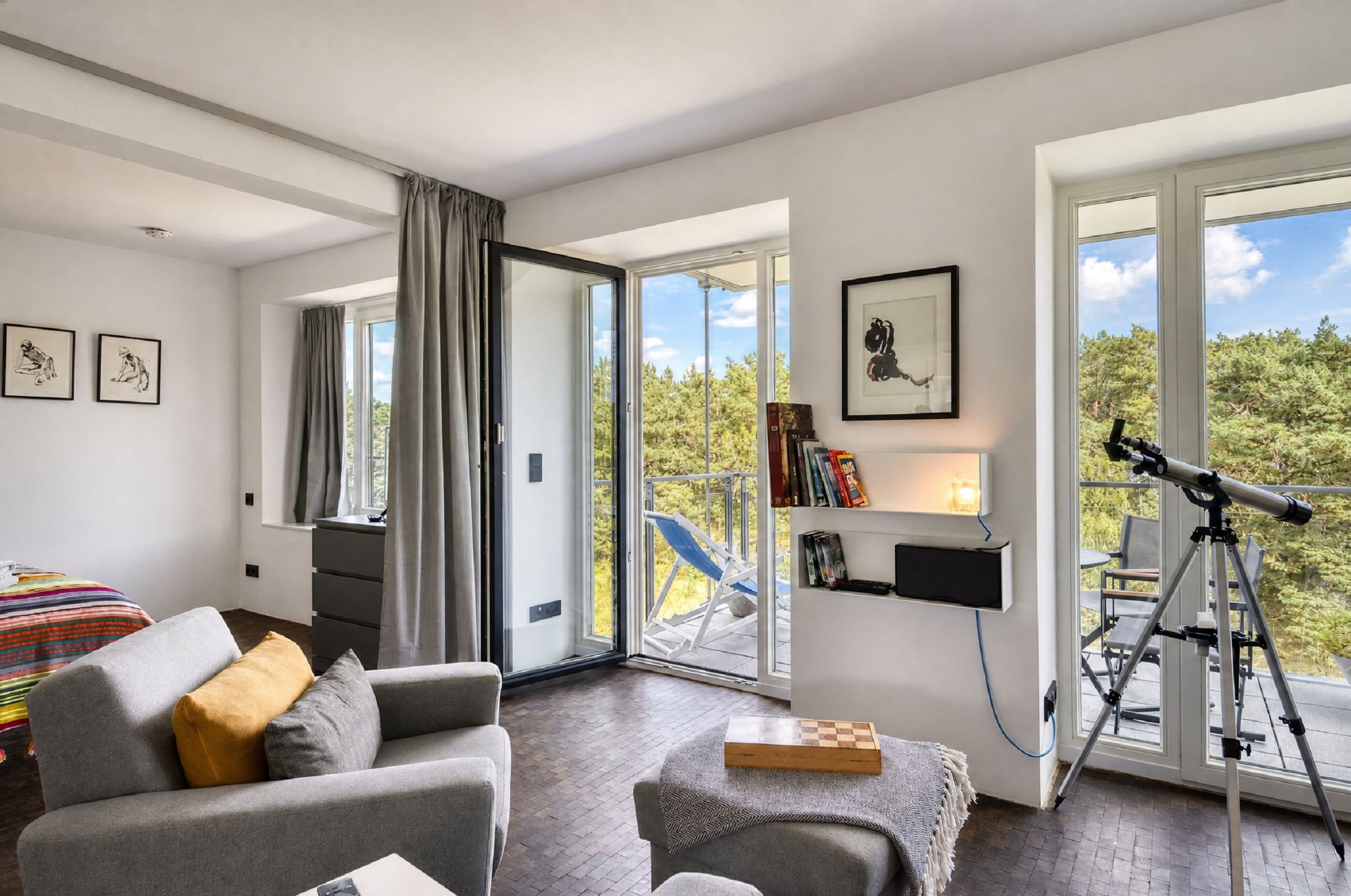 Una sala de estar moderna con un sofá, una mesa de centro, un telescopio y un balcón con vistas a árboles.