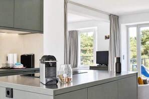 A modern kitchen with a built-in coffee machine, a glass container with coins, and a view of the outdoors through large windows.
