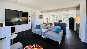 A modern living room with a large TV, two sofas, a coffee table, and a dining area with chairs and a table.