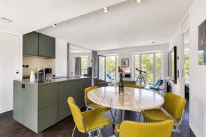 A modern kitchen with a central island, dining area with yellow chairs, and large windows offering a view of trees.