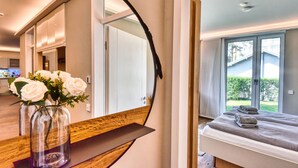 Ein modernes Schlafzimmer mit einem großen Spiegel, einem Bett mit kariertem Überwurf und Blick auf ein Haus durch ein Fenster.