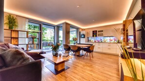 Ein modernes Wohnzimmer mit Sofa, Couchtisch und Essbereich. Im Hintergrund befindet sich eine Küche mit Schränken und einer Arbeitsplatte.