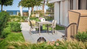 Eine Terrasse im Freien mit Tisch und Stühlen, umgeben von Grünpflanzen und Blick aufs Meer.