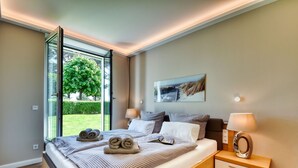 A modern bedroom with a large bed, two bedside tables, a window, and a view of greenery. - Baltic Sea vacation in Meeresrauschen 2 / Villa Vogue Binz: Sea view and front row (Binz)