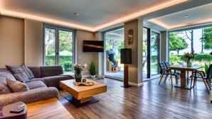 A modern living room with a sofa, coffee table, TV, and dining area with chairs and a table. - Baltic Sea vacation in Meeresrauschen 2 / Villa Vogue Binz: Sea view and front row (Binz)