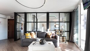 Ein modernes Wohnzimmer mit einem grauen Sofa, einem weißen Couchtisch und einem großen Fenster mit Vorhängen.