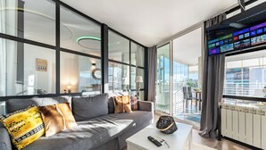 Ein modernes Wohnzimmer mit einem grauen Sofa, einem kleinen weißen Tisch und einem großen Fernseher, der eine Streaming-Dienstanwendung anzeigt.