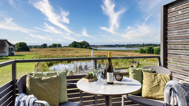 Ein Balkon mit einem Tisch für zwei Personen mit Blick auf einen See und Felder.
