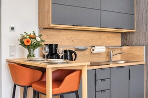 Une cuisine de taille réduite avec un plan de travail en bois, deux chaises orange, un évier et une machine à café.