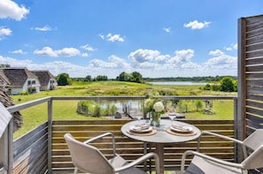 Un balcon avec une table dressée pour deux personnes, donnant sur un lac et un paysage verdoyant.