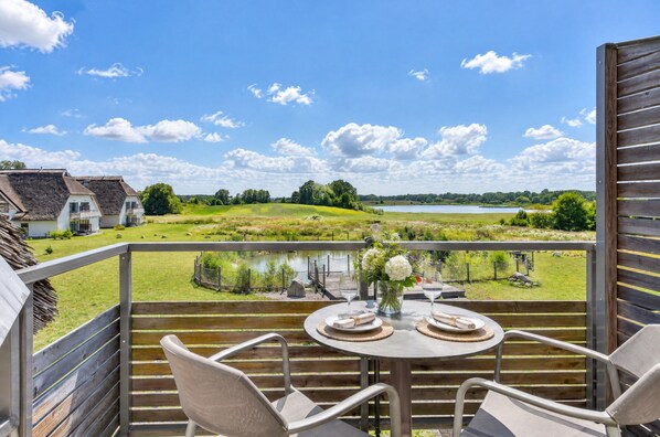 Een balkon met een tafel voor twee personen, met uitzicht op een meer en een groene omgeving.