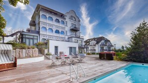 Una villa con piscina, mobiliario exterior y una escalera que conduce a los pisos superiores.